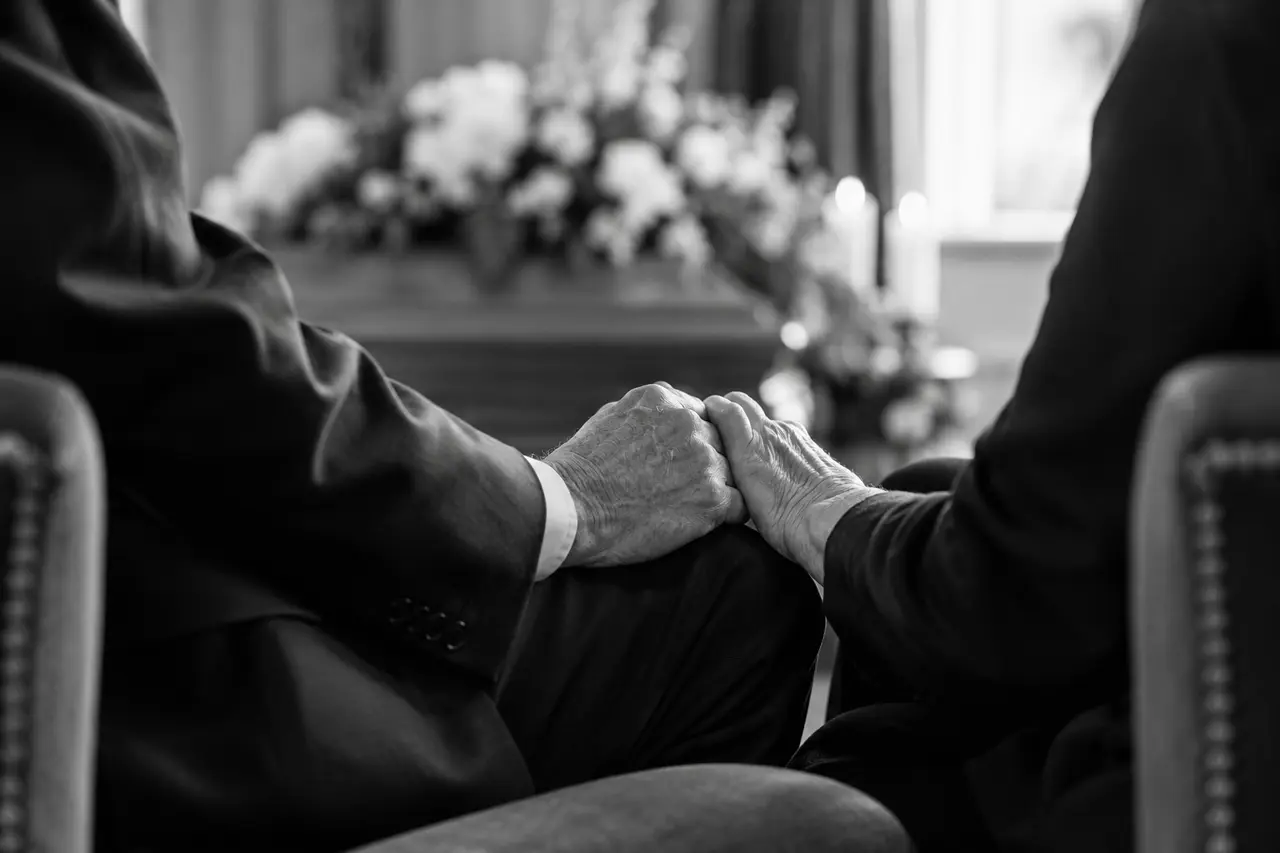 Illustrative photograph of two people holding hands during a memorial gathering
